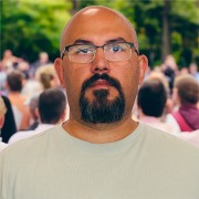Unsmiling bald man with glasses and dark moustache and goatee